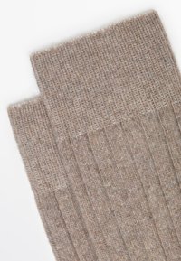 Calzini beige a coste realizzati in morbido tessuto, caratterizzati da una texture liscia e una banda leggermente più scura nella parte superiore per un contrasto aggiuntivo.