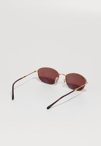 Sunglasses s okvirom od zlatnog metala, smeškanim pravokutnim staklima u smeškastoj boji i tamnim školjkastim zakrivljenim drškama na beloj pozadini.