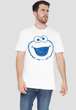 White cotton t-shirt featuring a blue graphic of a smiling cartoon character's face, with large eyes and textured detailing.