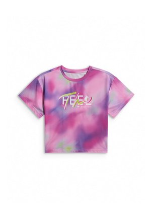 Młoda dziewczyna stoi, ubrana w różowo-fioletową koszulkę tie-dye, jednolite fioletowe szorty, białe skarpetki i czarne trampki na szarym tle.