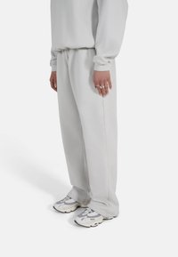 Lys grå joggebukser med en avslappet passform, elastisk midje og sidelomme detaljer, kombinert med klumpete grå sneakers.