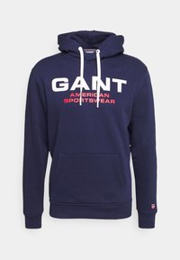 Sudadera con capucha azul marino de mezcla de algodón, con texto en blanco y rojo "GANT AMERICAN SPORTSWEAR" y un bolsillo delantero.