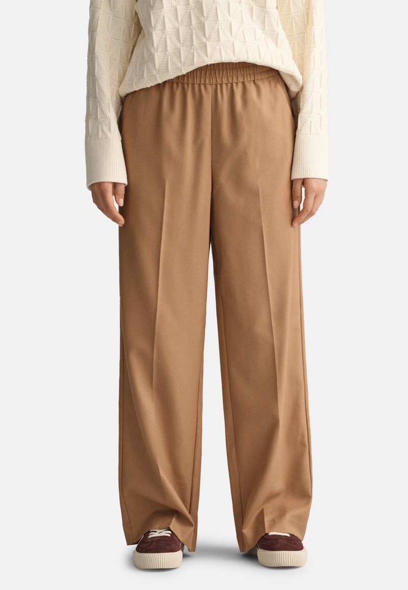 Bruine wijde broek van zacht materiaal, met een elastische tailleband. Gecombineerd met donkerrode sneakers en een gestructureerde witte trui.