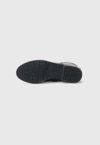 Zwarte sneakerzool van rubber. Bevat een getextureerd grippatroon en een logo dat nabij de hiel is geperst. Gladde bovenranden.