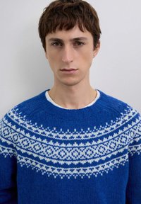 Suéter de punto en azul vibrante con un patrón geométrico Fair Isle blanco alrededor del escote y los hombros, con un diseño de cuello redondo.