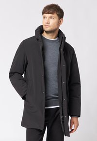 Czarny ocieplany płaszcz z zamkiem z przodu, wysokim kołnierzem i detalami na zatrzaski. Prezentuje gładką fakturę i lekko tapered fason.