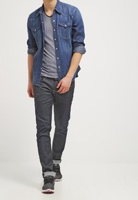 Denimskjorte i mørkeblå, gråstribet t-shirt, grå jeans, sorte sportsko med hvide accenter, optrukne ærmer og forlommer på skjorten.
