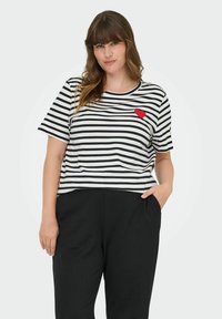 Stripete t-skjorte med kort erme i svart og hvitt med et rødt hjerte på brystet, kombinert med svarte bukser. Myk, avslappet passform.