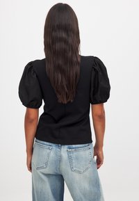 Top negro de mangas abullonadas con un cuerpo ajustado y una textura suave, combinado con jeans de denim de color azul claro y desgastado que presentan bolsillos traseros visibles.