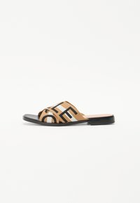 Mules en textile marron avec bout ouvert. Dotées d'un motif géométrique diagonal noir et blanc sur le dessus et d'une semelle noire plate.