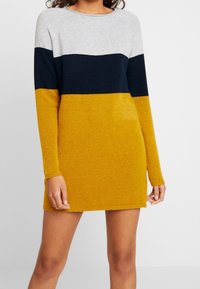 Abito in maglia con scollo rotondo, caratterizzato da righe orizzontali in grigio, blu navy e giallo senape. Texture morbida, maniche lunghe e vestibilità comoda.