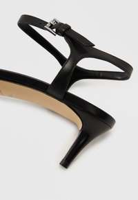 Μαύρο δερμάτινο σανδάλι με λεπτό λουράκι στον αστράγαλο, ανοιχτή μύτη και τακούνι στιλέτο 7 εκ., με λείο μπεζ πέλμα.