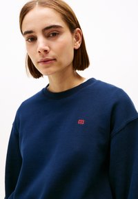Navyblauwe sweatshirt van zachte stof, met een ronde halslijn en een klein rood logo op de linker borst. Eenvoudig en klassiek ontwerp.