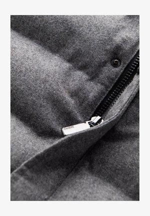 Grijze opblaasbare jas van stof met een zachte textuur, voorzien van een ritssluiting, zwarte accenten en een metalen label met de naam "OMBRA."