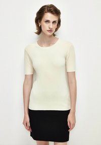 Top corto de canalé en color crema con cuello redondo, combinado con una falda negra ajustada. La tela parece suave y elástica.