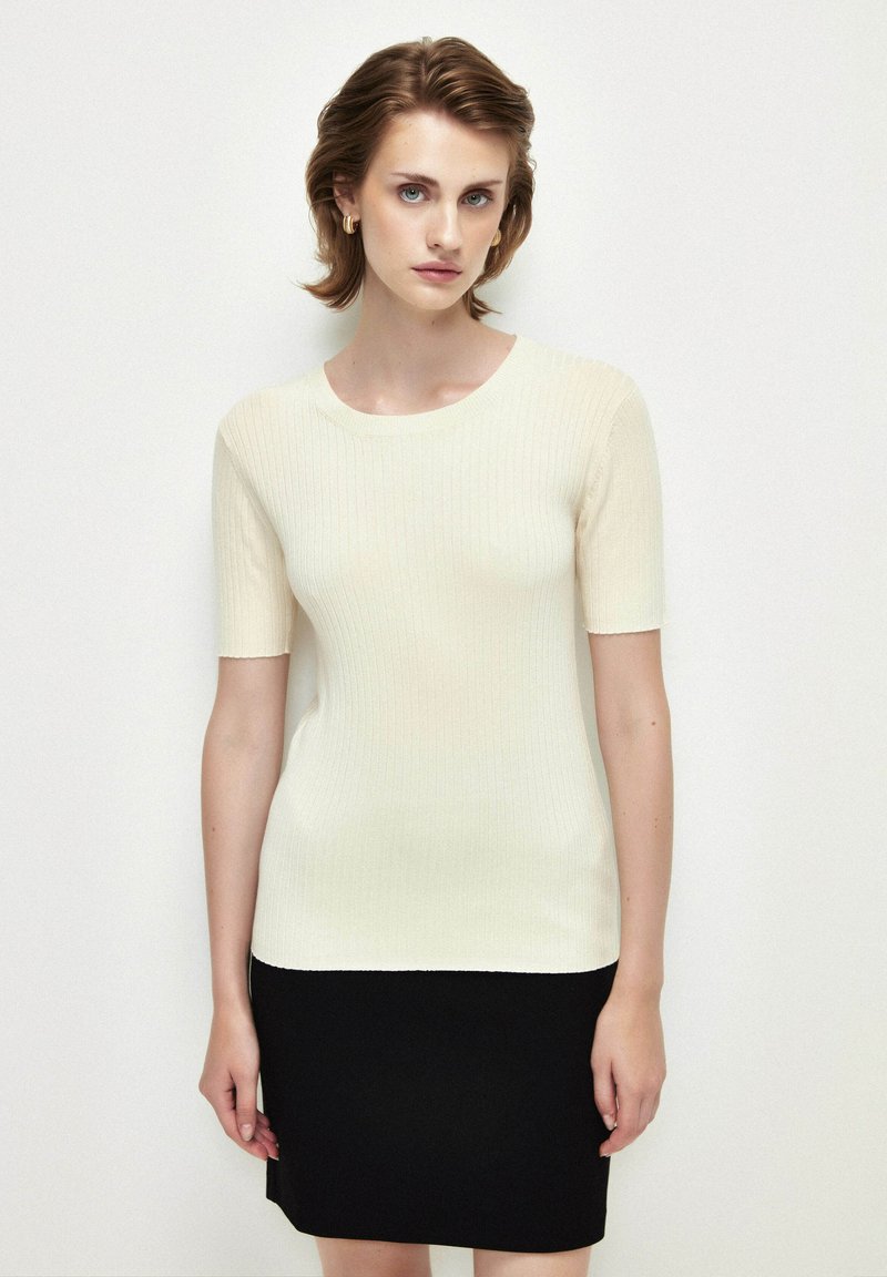Top corto de canalé en color crema con cuello redondo, combinado con una falda negra ajustada. La tela parece suave y elástica.