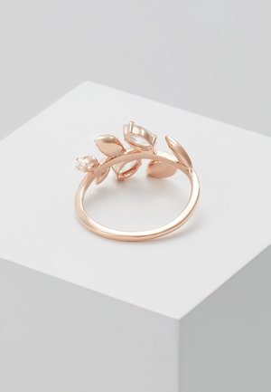 Anello in oro rosa con dettagli a forma di foglia e piccoli cristalli su una fascia liscia, esposto su un piedistallo a cubo bianco.