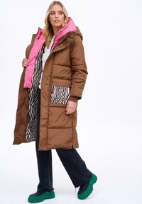 Brązowa kurtka puchowa z różowym kapturem i podszewką w zebrę, z kieszenią w zebrę, zielonymi detalami i długim krojem.