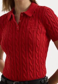 Polo shirt en tricot rouge avec un motif de câble texturé, manches courtes et une patte de boutonnage à trois boutons ornée d'un logo brodé.