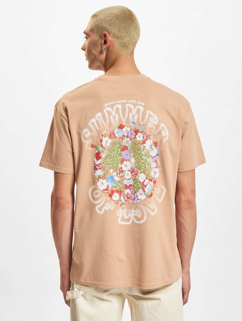Beige bomullstrøye med et blomsterdesign i livlige farger og hvit tekst på baksiden. Korte ermer, avslappet passform.