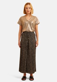 Top à bretelles spaghetti en or métallique avec un décolleté en V ; jupe plissée noire avec un motif floral ; sandales plates noires.