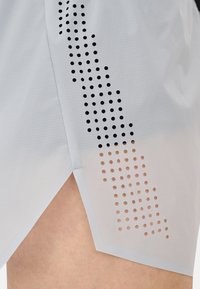 Leichte sportliche Shorts in Grau, mit einem Verlauf von schwarzen bis transparenten Perforationen an der Seite und einem seitlichen Schlitz für mehr Beweglichkeit.