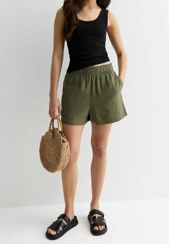 Débardeur noir, short à taille élastique vert olive, sac à main en paille tressée et sandales noires avec un design à lanière épaisse.