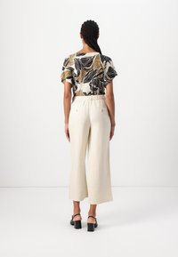 Blusa floreale multicolore con maniche corte e schiena ampia e aperta; pantaloni crema a gamba larga con vita elasticizzata e tasche; scarpe nere con tacco a blocco.