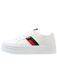 Baskets en toile blanches avec une semelle plateforme, dotées d'un accent rayé vert et rouge et d'une étiquette de logo noire près des lacets.