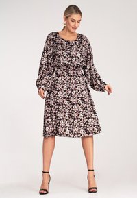 Kwiatowa sukienka z długimi, balonowymi rękawami, na czarnym tle, z różowymi i białymi kwiatami. Dopasowana w talii, o długości do kolan. W zestawie z czarnymi sandałami na obcasie.