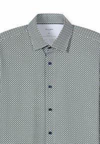 Weißes Hemd mit geometrischem Muster aus kleinen schwarzen und grünen Kreisen. Mit spitzem Kragen und blauen Knöpfen. Modern geschnitten.