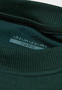 Ciemnozielony sweter z kołnierzem o prążkowanej fakturze, z haftowaną metką marki "Intimissimi Uomo" w jasnoszarym kolorze na miękkim materiale.