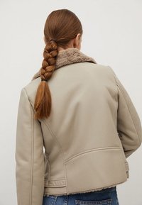 Giacca di pelle beige con colletto in pelo sintetico, caratterizzata da un design aderente e dettagli di cucitura visibili. La vista posteriore mette in risalto la texture e la forma.