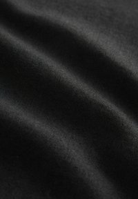 Zwarte stof met een zachte, gladde textuur, met subtiele kreukels en plooien. Het materiaal lijkt lichtgewicht en uniform van kleur.