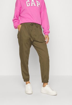 Groene joggingbroeken met een elastische tailleband en boorden. Gecombineerd met een felroze sweatshirt met "GAP" in witte letters. Witte sneakers.
