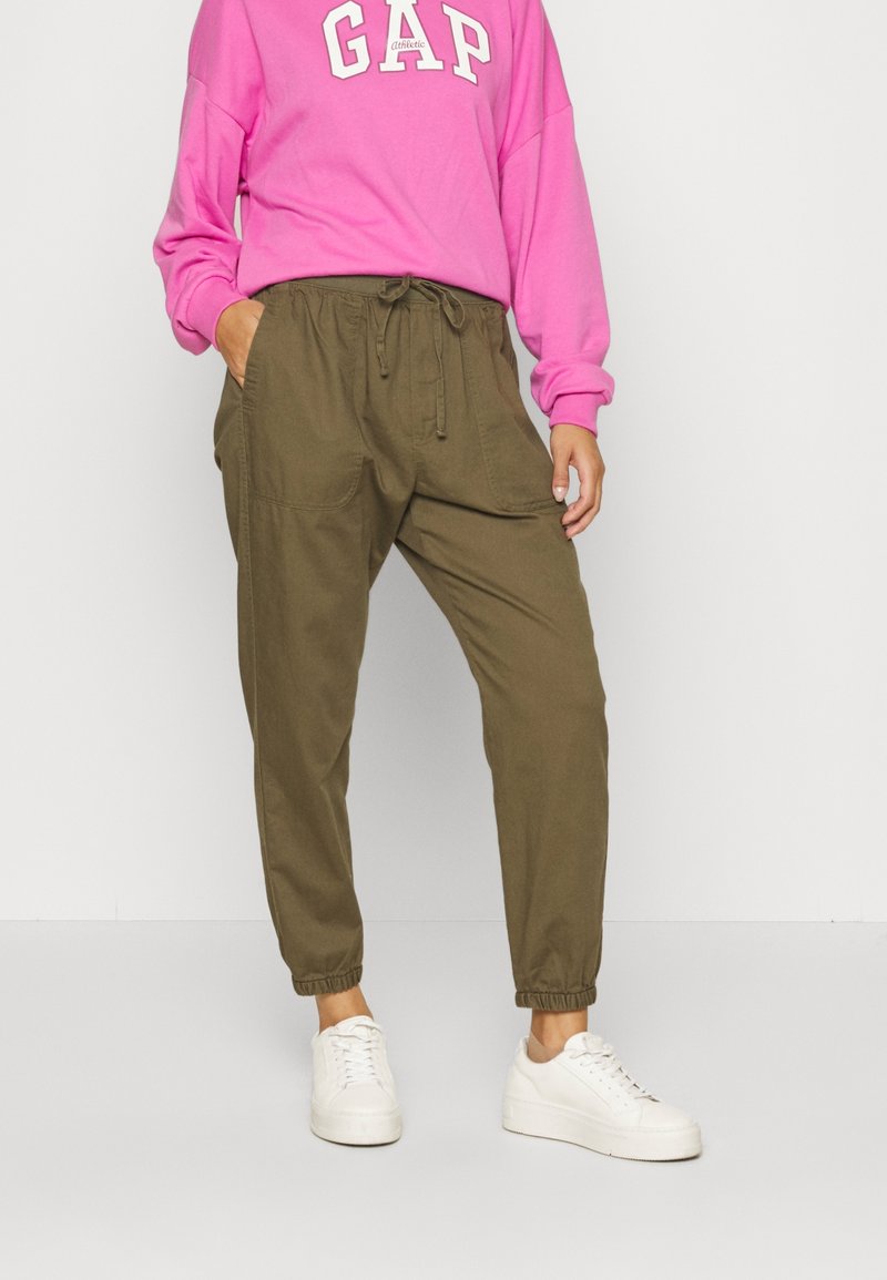 Grüne Jogginghose mit elastischem Bund und Bündchen. Kombiniert mit einem leuchtend pinken Sweatshirt mit "GAP" in weißen Buchstaben. Weiße Turnschuhe.