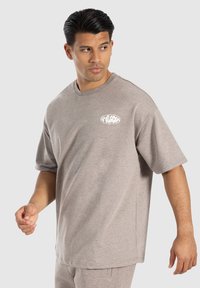 Kortærmet beige t-shirt lavet af blødt stof. Den har en rund halsudskæring og et lille hvidt logo på venstre bryst. Løs pasform.