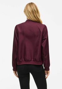 Burgunderfarget sateng bomberjakke med lange ermer, rund hals og elastisk kant. Glatt tekstur med en løs passform.