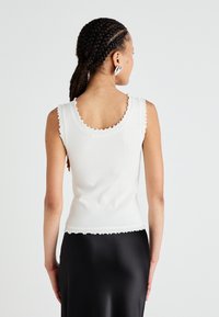 Débardeur blanc à côtes avec des bords festonnés, design ajusté et dos plongeant. Associé à une jupe en satin noir.