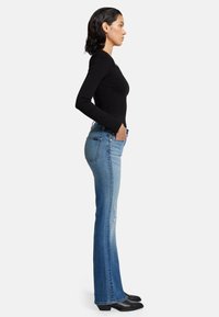 Flared jeans van lichtblauw denim met lichte slijtage, gecombineerd met een strak zwart shirt met lange mouwen, gezien vanaf de zijkant.
