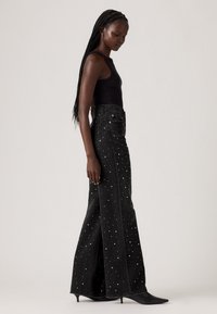 Zwarte denim maxi rok met split, versierd met verspreide strass-accenten. Draag het met een zwarte tank top en puntige hakken.