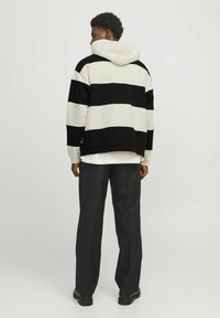 Hoodie rayé noir et blanc avec une poche kangourou à l'avant, manches longues et capuche, associé à un pantalon ample sombre et des chaussures noires.