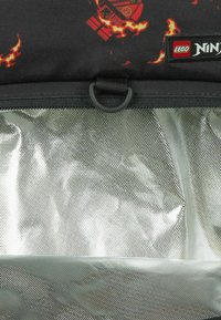 Zwarte LEGO Ninjago-rugzak met rood vlamontwerp, transparante voorzak en zwarte D-ring onder het logo-label.