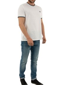 White short-sleeve t-shirt with black ribbed collar and cuffs, featuring a small logo on the left chest. Paired with light blue denim jeans.