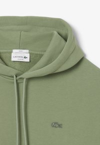 Felpa verde menta con un taglio ampio, dotata di cappuccio regolabile con lacci e logo ricamato sul petto. Materiale morbido in misto cotone.
