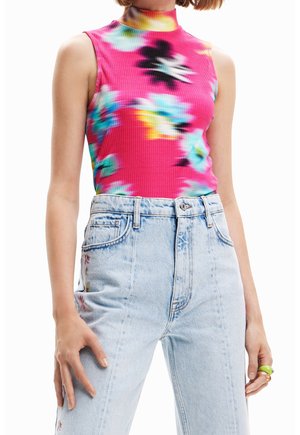 Ärmelloses, hochgeschlossenes pinkes Oberteil mit mehrfarbigem Batikmuster, kombiniert mit hoch taillierten hellblauen Jeans mit seitlicher Blumenstickerei.