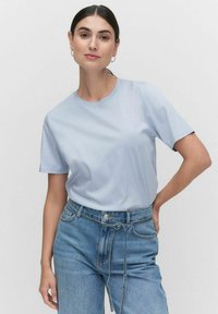 Vaalean sininen lyhythihainen T-paita pyöreällä kaula-aukolla, sileä tekstuuri, yhdistettynä korkeavyötäröisiin sinisiin farkkuihin, joissa on solmittava yksityiskohta vyötäröllä.