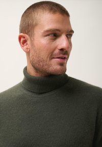 Zielony sweter z golfem wykonany z miękkiej dzianiny, z wysokim prążkowanym kołnierzem i gładką fakturą, dopasowany krój.