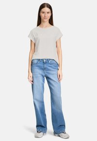 Lys grå bomulds t-shirt med opsmøgede ærmer, der har et subtilt grafisk design. Mødt med lyseblå brede jeans og grå sneakers.