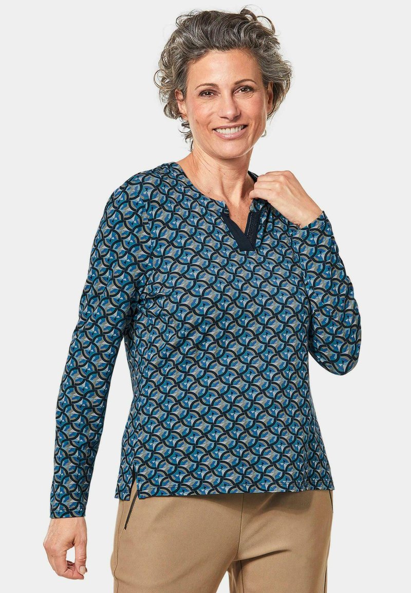 Langärmliges Oberteil in Blau mit einem geometrischen Muster aus Kreisen. V-Ausschnitt-Design mit kontrastierenden marineblauen Akzenten und seitlichen Schlitzen für mehr Komfort.
